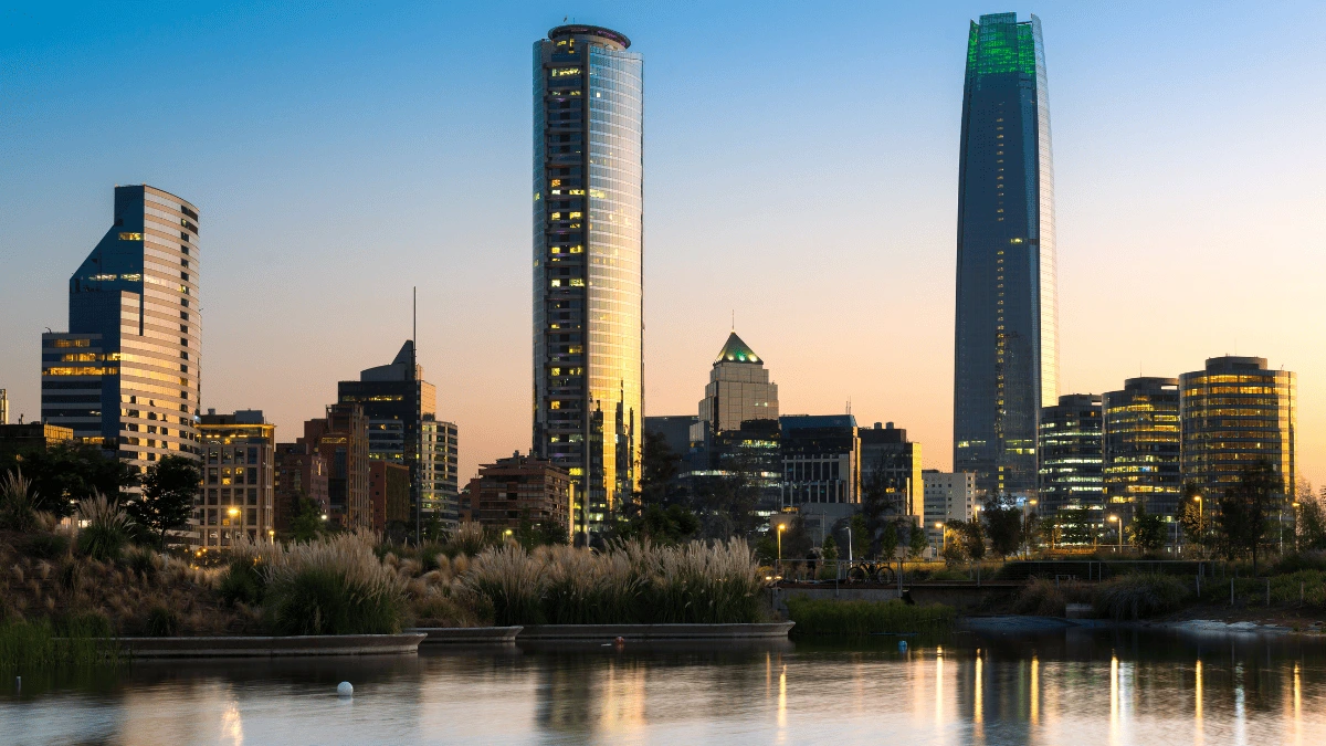 Skyline de Santiago de Chile al atardecer con modernos rascacielos reflejados en un cuerpo de agua.