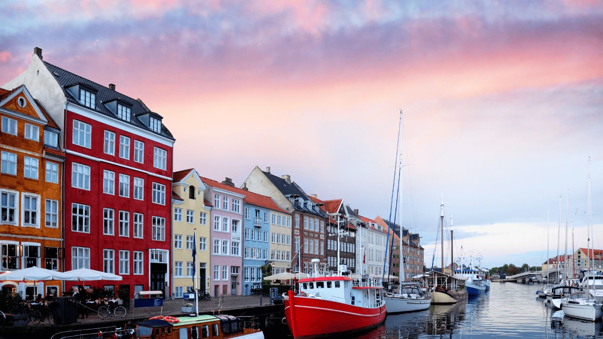 Coloridas casas junto al canal de Nyhavn en Copenhague, Dinamarca, con barcos atracados y un cielo al atardecer.